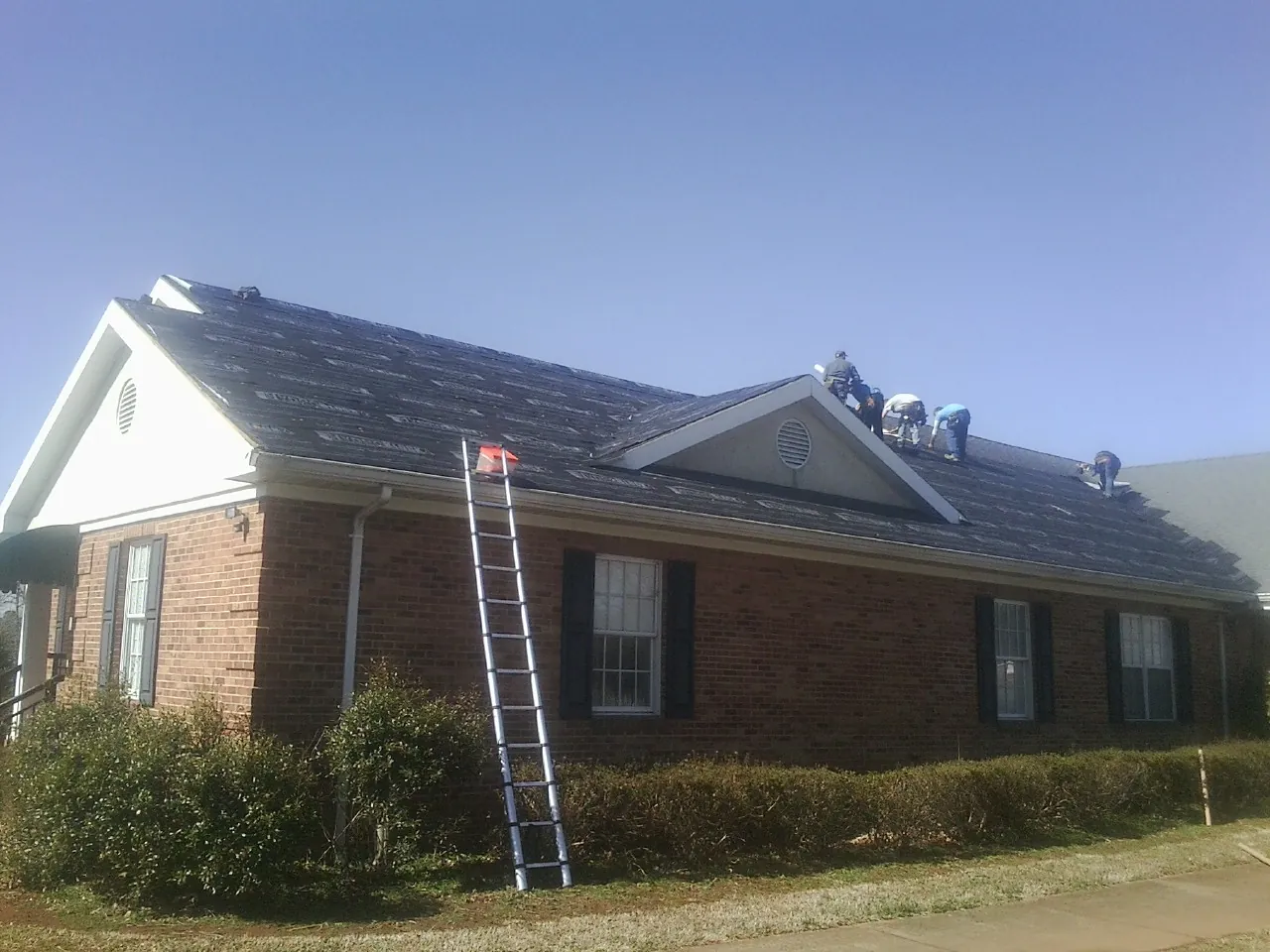 Crew tearing shingles off a brick ranch roof with a ladder set — Metal Roof Repair work by our crew in Berlin