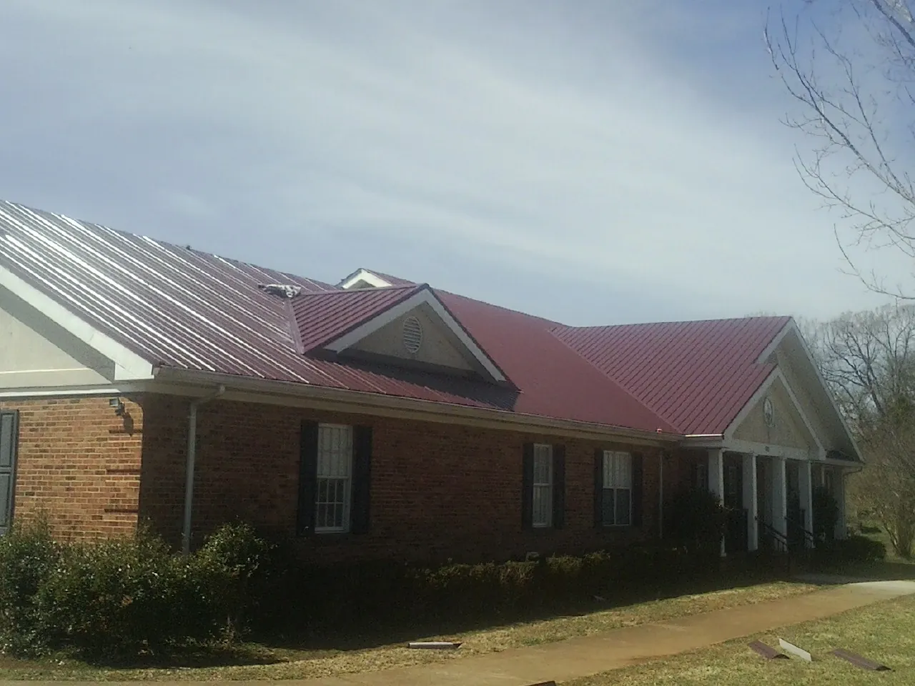 Red metal roof with gabled entries on a long brick building, from a Hail Damage Roof Repair job in Berlin