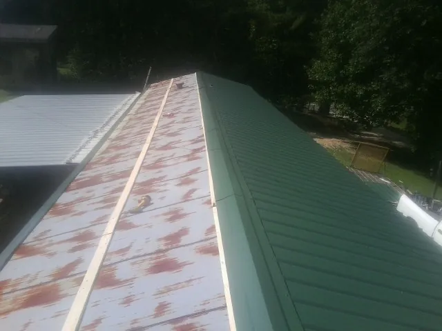 Old rusted panels beside newly installed green metal roofing — Wind Damage Roof Repair by Roofing Brothers in Berlin